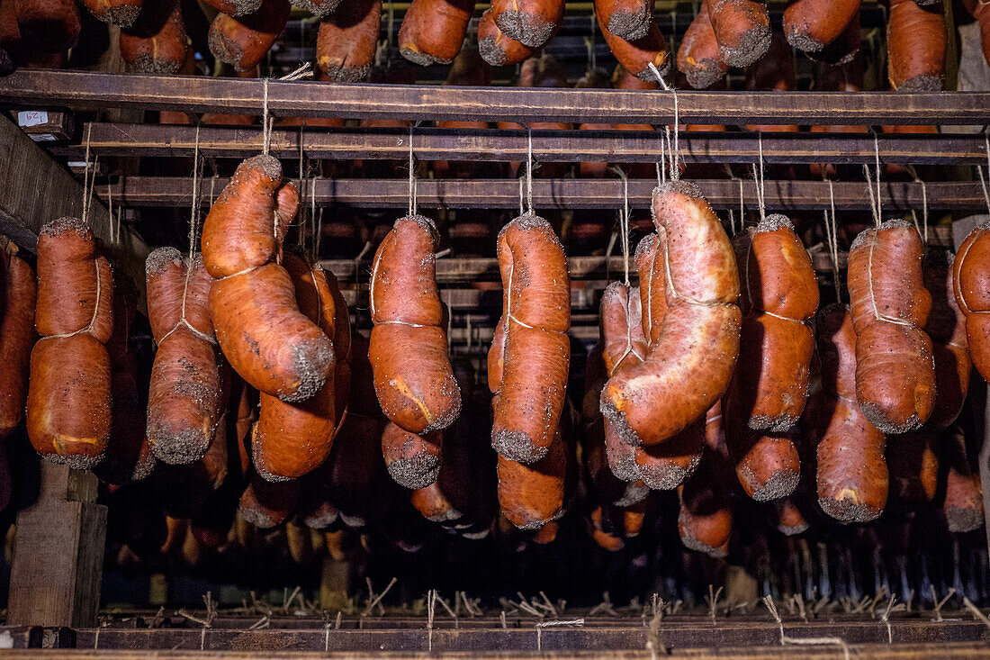 The image captures a range of cured sausages, including sobrasada, finely aged in a drying room. The sausages display a rich red color indicative of the paprika used in their preparation.