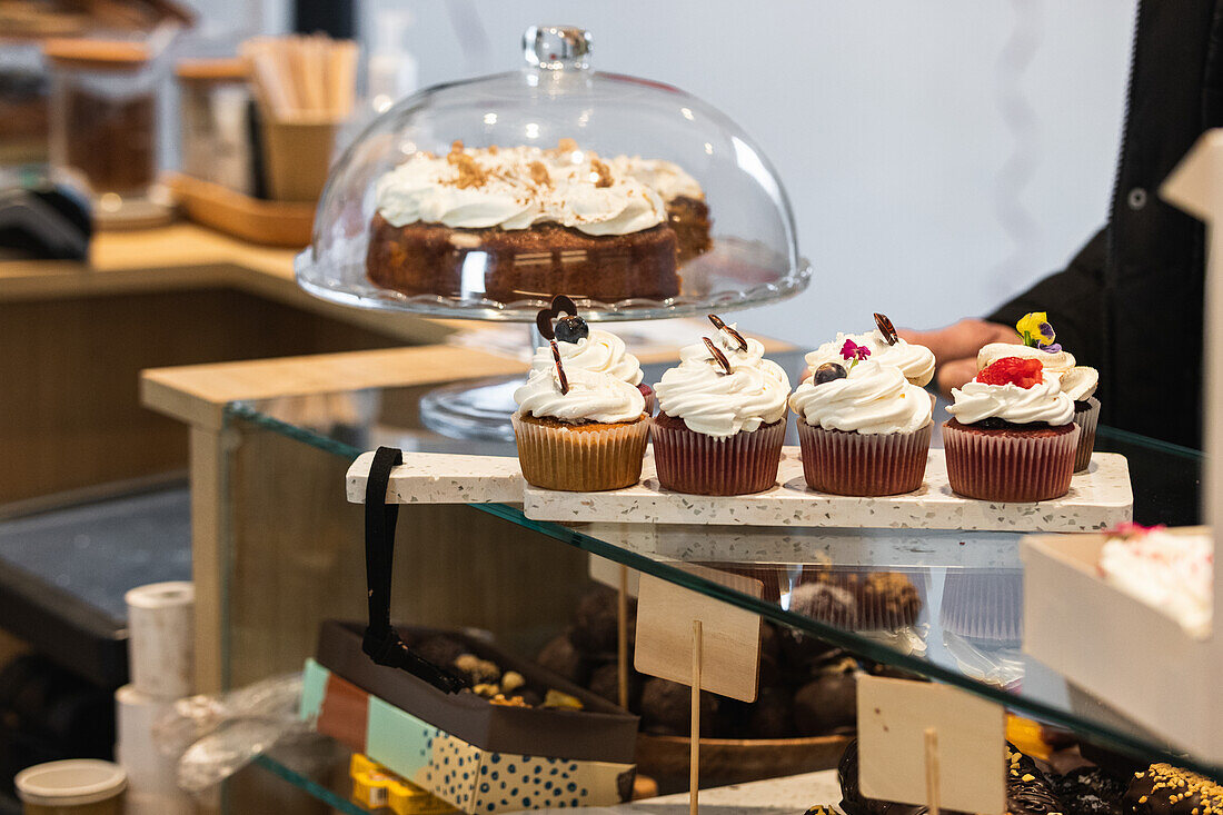 Verschiedene süße vegane Cupcakes auf einem Schneidebrett in einer Glasvitrine in der Backstube