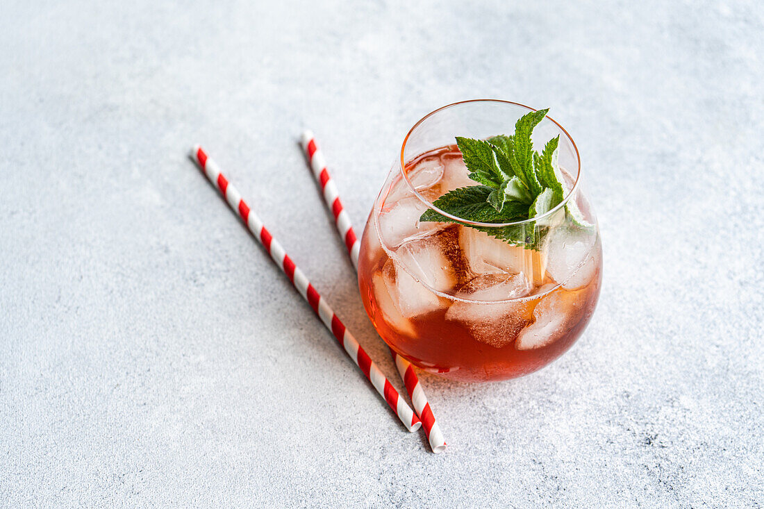 Von oben ein erfrischendes Glas Cola-Cocktail, garniert mit frischen Minzblättern und serviert mit rot-weiß gestreiften Strohhalmen, auf einer strukturierten grauen Oberfläche. Ideal für sommerliche Erfrischungen und Partygetränke.