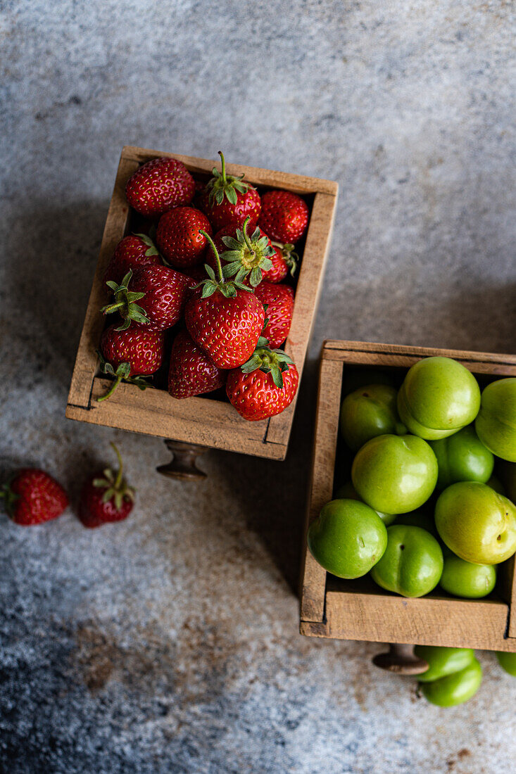 Vintage wooden boxes filled with a selection of organic ripe strawberries, green plums, and sweet cherries on a textured background