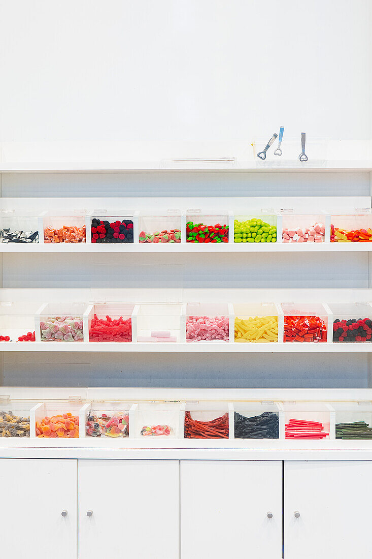 A well-organized candy shop interior with assorted candies sorted in transparent bins on white shelves against a clean background