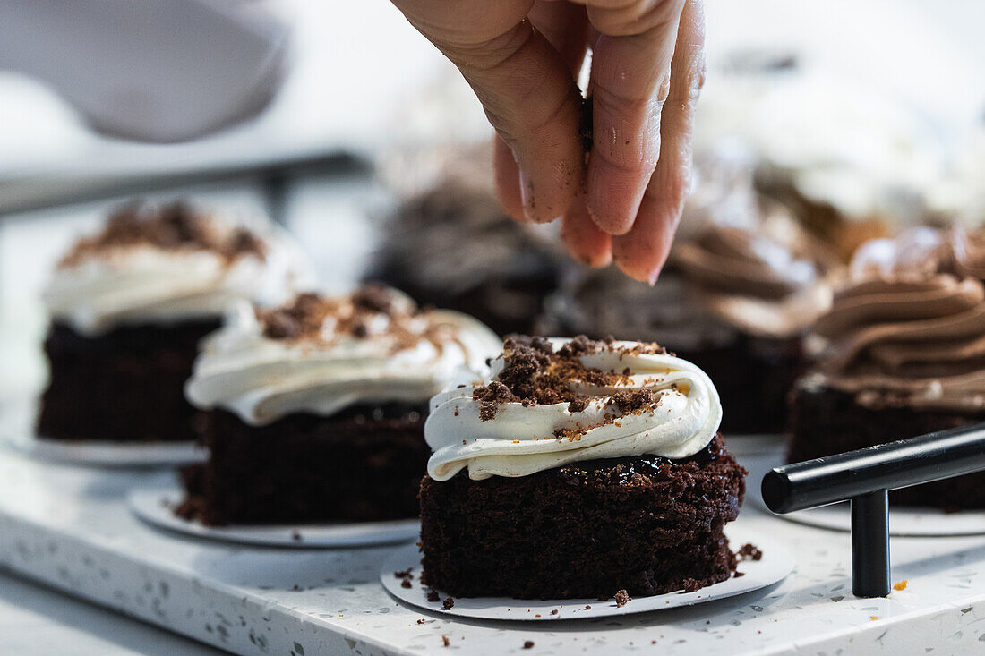 Unbekannter Erntekoch bestreut appetitlichen veganen Biskuitkuchen mit Schokolade, während er in der Küche einer Bäckerei kocht