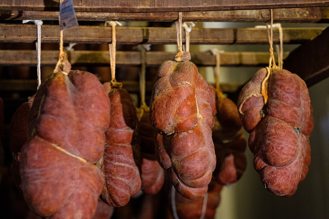 Selection of cured meats, with a focus on Sobrasada sausages, traditionally made from pork and spices, suspended in a shop under warm lighting.