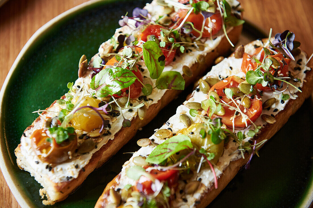 Nahaufnahme einer frisch zubereiteten Bruschetta mit buntem Belag auf einem dunkelgrünen Teller, der eine Mischung aus Aromen und Farben für eine einladende Mahlzeit bietet.