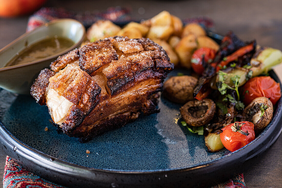 Saftiges gebackenes Schweinefleisch in einer reichhaltigen Honigsauce, begleitet von einem bunten Salat mit gegrilltem Gemüse, einschließlich Tomaten und Pilzen, serviert auf einem dunklen Keramikteller