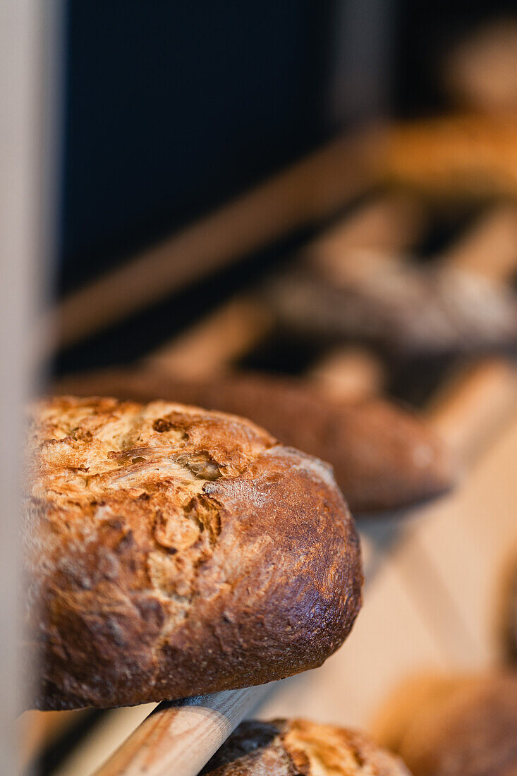 Frisch gebackenes, handwerklich hergestelltes Sauerteigbrot mit goldener Kruste, ausgestellt auf einem Holzregal, das die Schönheit hausgemachter Backwaren präsentiert.