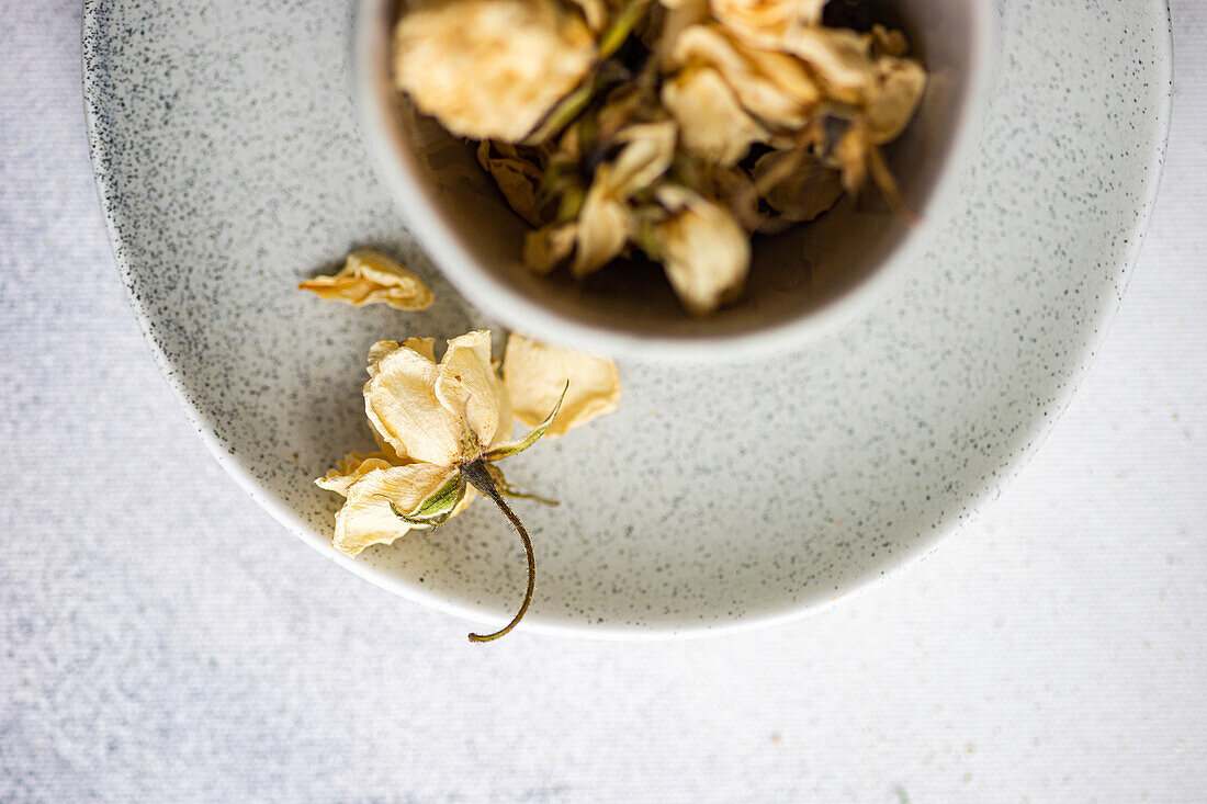 A delicate, dried rose rests inside a speckled ceramic bowl, set against a white linen background, evoking a serene and minimalist aesthetic