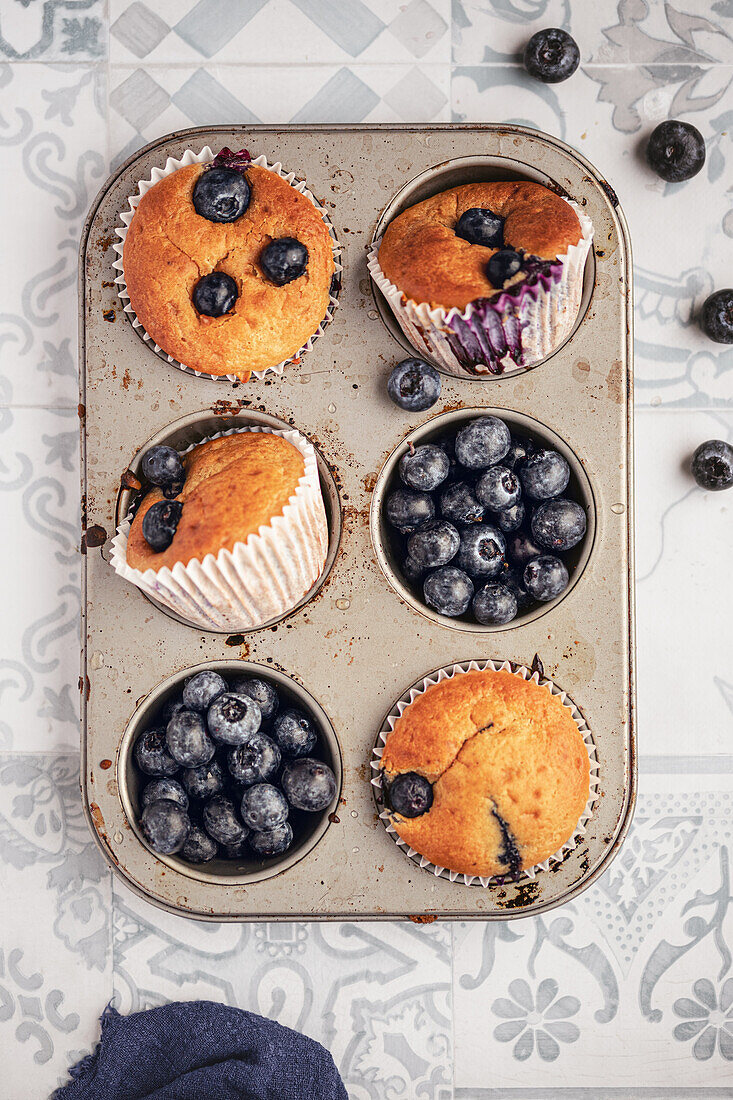 An appetizing image displaying freshly baked blueberry muffins and whole blueberries in a rustic muffin tin