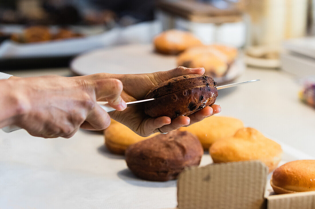 Unrecognizable crop baker cutting chocolate sponge cake with knife while cooking delicious vegan desserts in bakehouse