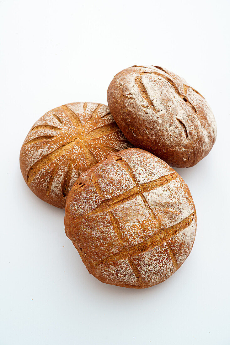 A duo of artisanal sourdough bread loaves with a dusting of flour, showcased against a white background.