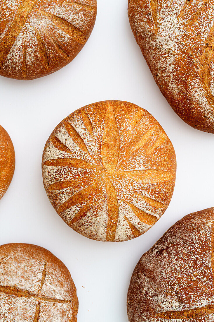 A selection of handcrafted sourdough breads with golden crusts dusted with flour on a pristine white background.