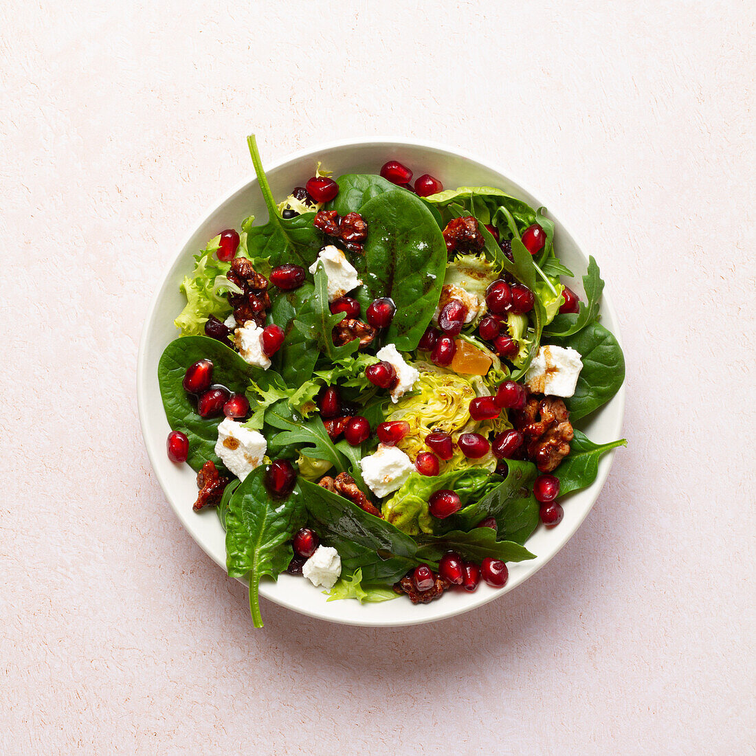 A vibrant winter salad featuring candied walnuts, juicy pomegranate seeds, mixed greens, creamy goat cheese, cranberries, and a rich fig jam vinaigrette