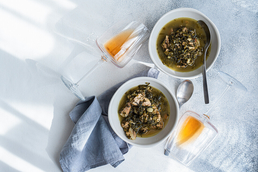 Top view of traditional Georgian dish, chakapuli, featuring stewed meat with white wine, tart green plums, and a mix of fresh herbs such as tarragon, coriander, parsley, and green onions, artfully presented.