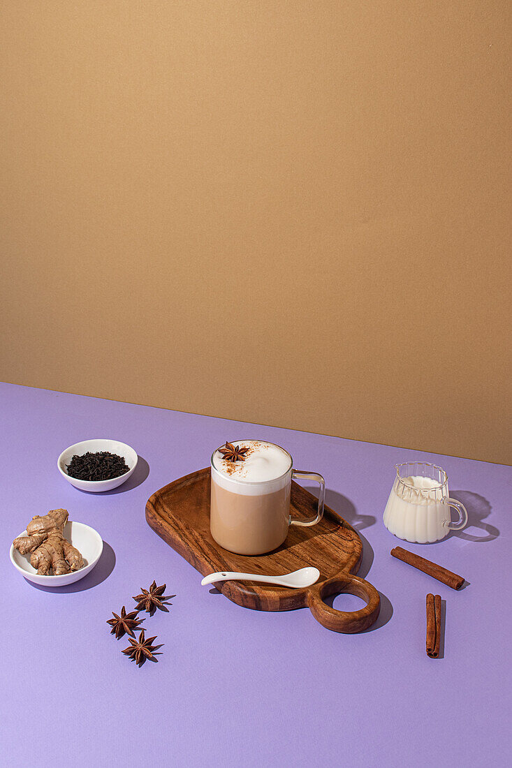 From above, Delicious chai latte with star anise on a wooden board surrounded by fresh ginger and tea leaves on a colorful backdrop