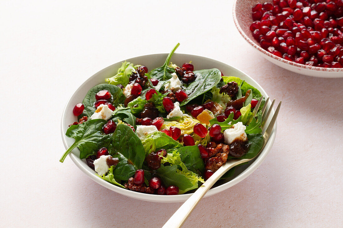 Eine köstliche Wintersalatschüssel mit verschiedenen Blattsalaten, bestreut mit Granatapfelkernen, kandierten Walnüssen, Ziegenkäse und Preiselbeeren, angemacht mit einer Feigenmarmelade-Vinaigrette