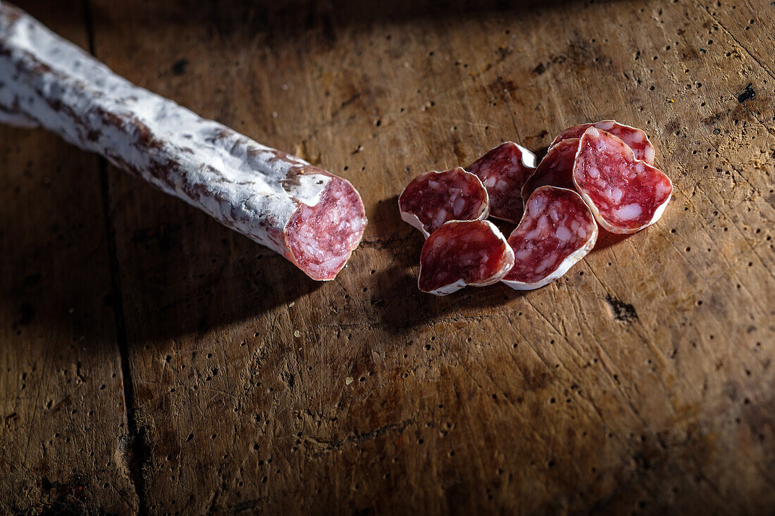 Close-up of sliced cured sausage alongside a whole fuet on a textured wooden surface, highlighting the rich textures and colors of the traditional meat.