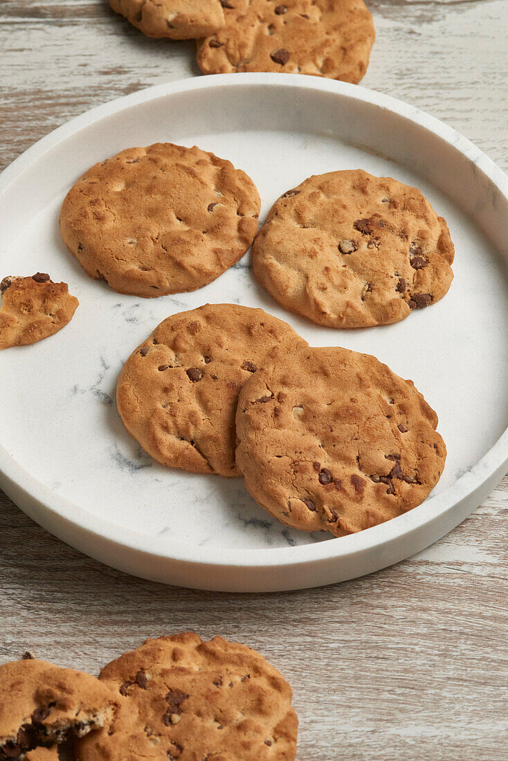 A close-up view of freshly baked chocolate chip cookies served on a round marble plate, with a rustic wooden table backdrop