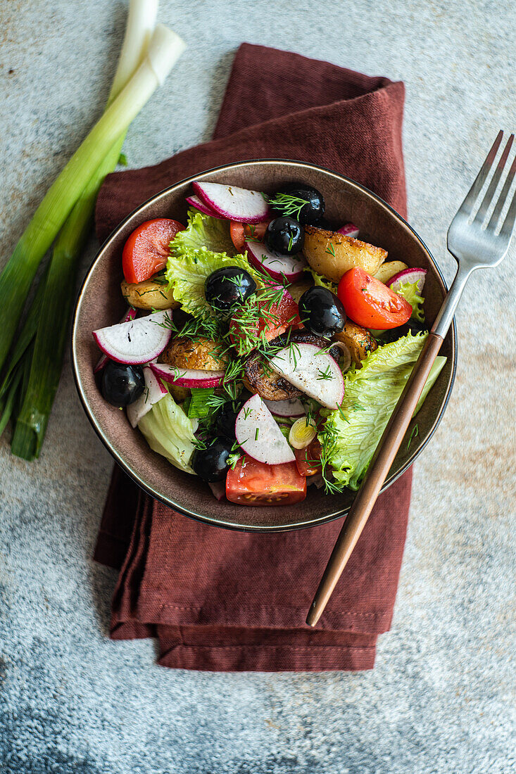 Top view of tantalizing Mediterranean salad elegantly presented with herbed roasted potatoes, juicy cherry tomatoes, olives, and crisp radishes, alongside fresh lettuce and spring onions