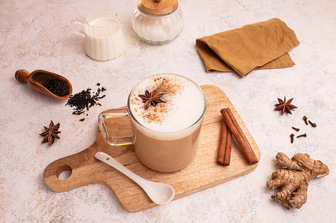 Von oben, im rustikalen Stil, ein köstlicher Chai Latte mit schaumiger Milch, Sternanis und Zimtstangen, präsentiert mit Teeblättern, Ingwer und Nelken.