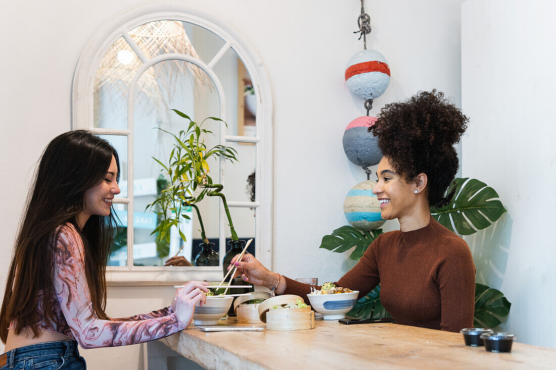 Side view of diverse female friends sitting at table and eating tasty poke while spending weekend in restaurant