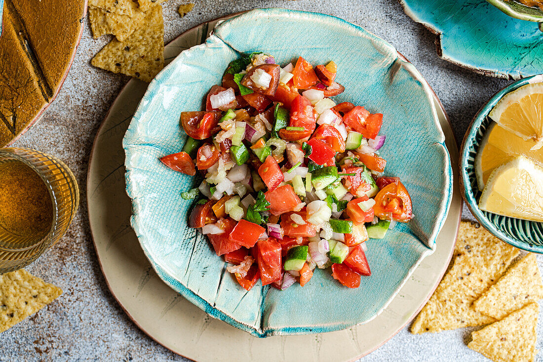 Draufsicht auf Pico de Gallo, eine klassische mexikanische Salsa aus frischen Tomaten, Zwiebeln, Koriander, grünem Paprika, Avocado und einem Spritzer Zitronensaft, serviert auf einem Keramikteller zusammen mit knusprigen Maischips