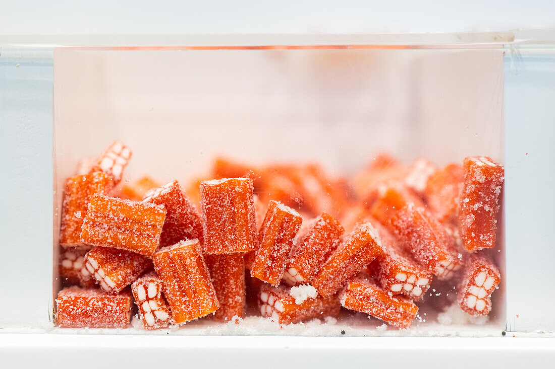 Close-up of juicy orange-flavored candy sticks coated with granulated sugar, displayed in a transparent jar