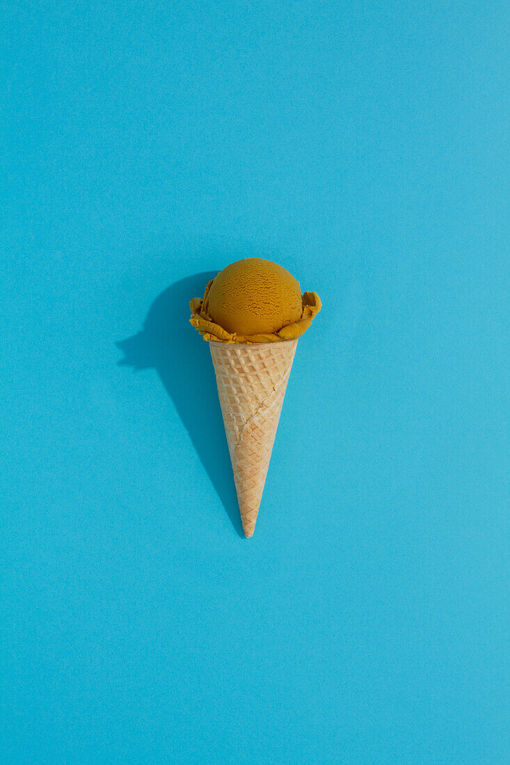 A vibrant Pistachio ice cream scoop sits atop a classic waffle cone against a blue background, casting a playful shadow