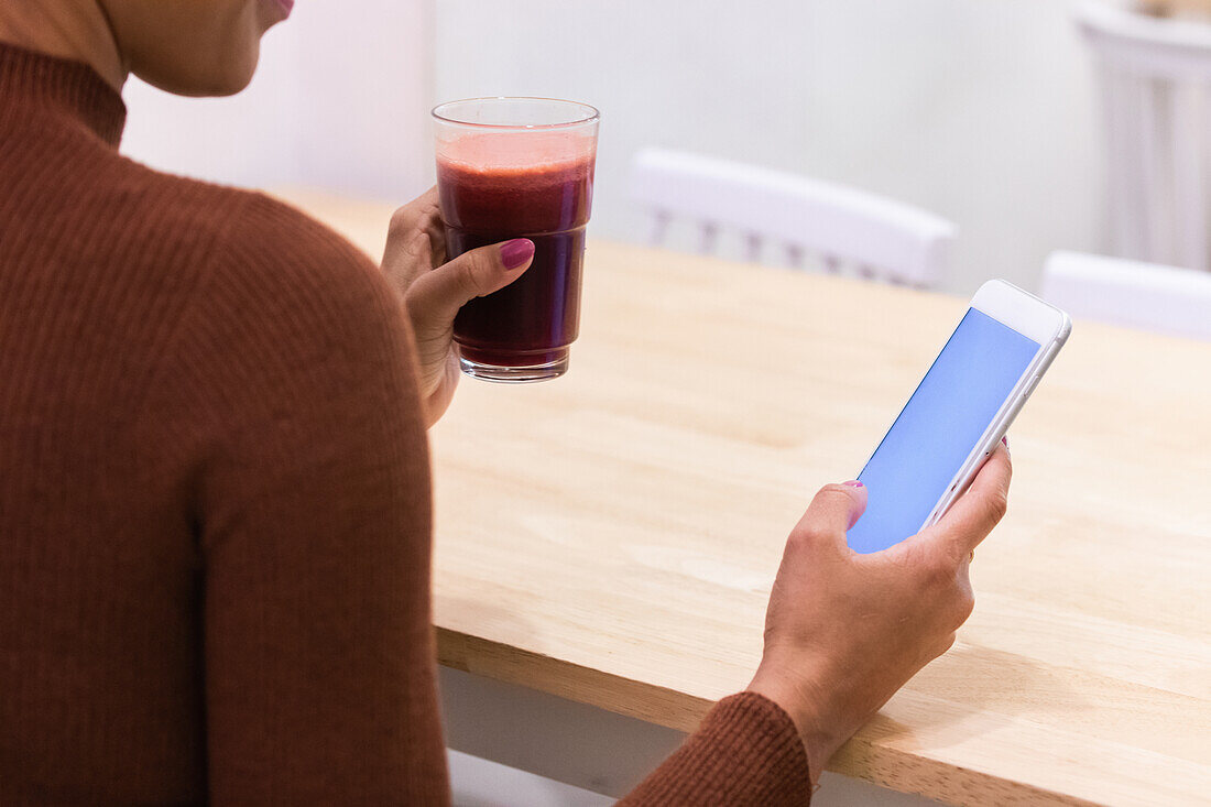 Cropped unrecognizable African American female freelancer browsing smartphone while sitting at table in cafe and working on remote project