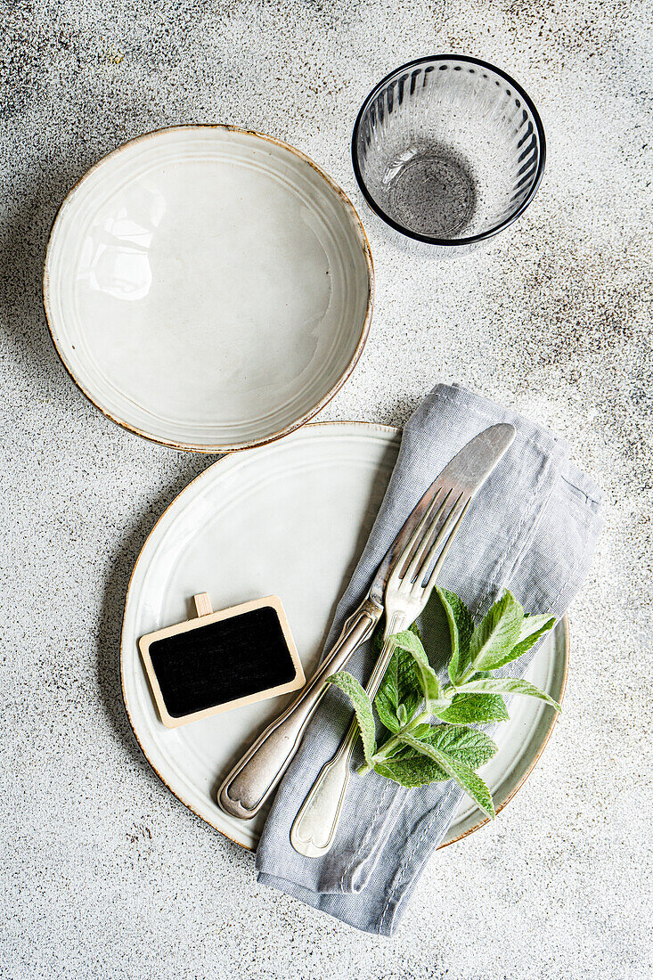 This image captures a beautifully arranged summer table setting featuring a soft color palette with mint leaves as a focal point, adding a refreshing touch to the elegant plates, silverware, and linen napkin