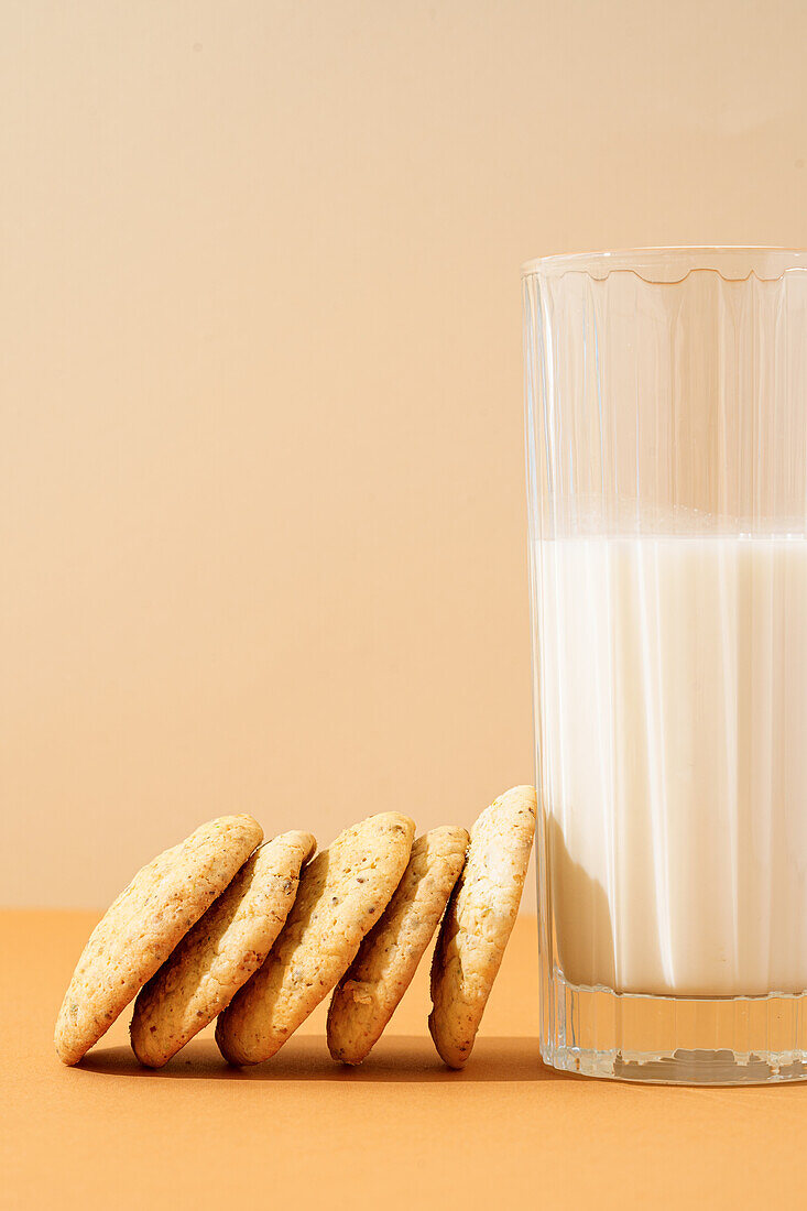 A warm, inviting arrangement of homemade walnut biscuits paired with a full glass of fresh milk showcased on a pastel background, evoking home-baked comfort.