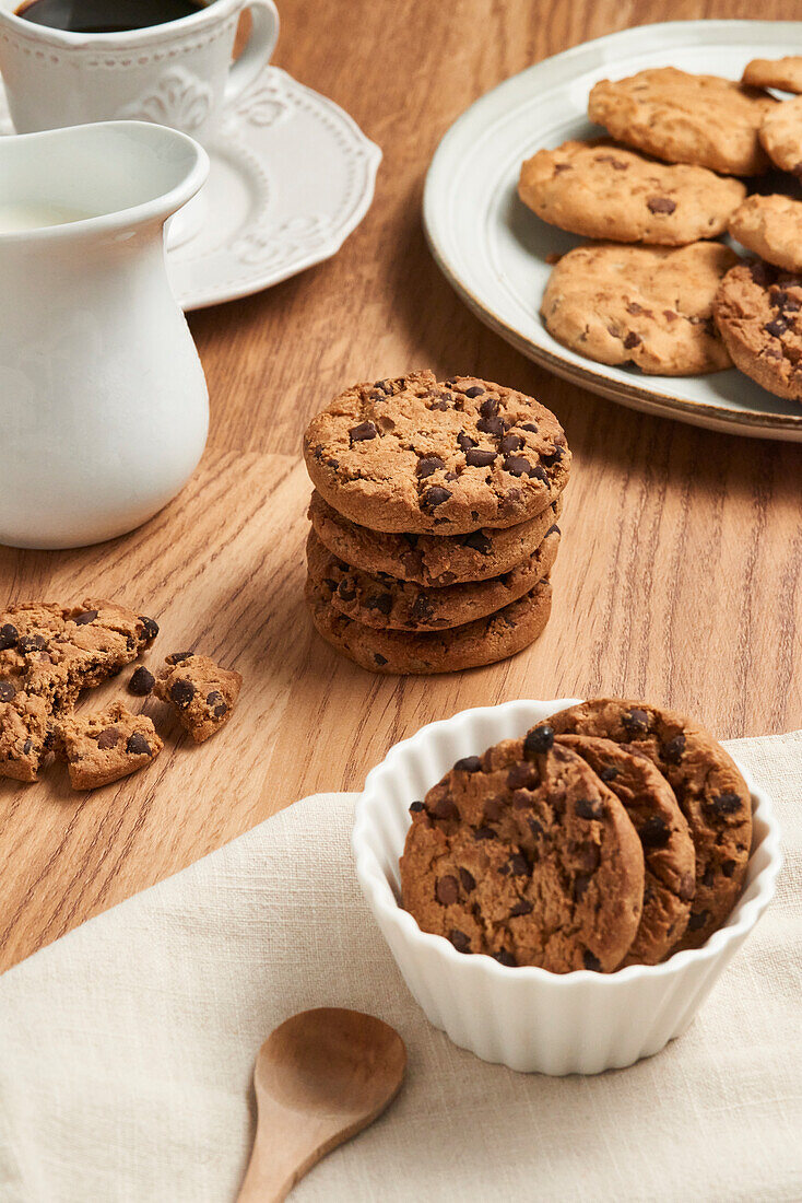 A top view of tasty chocolate chip cookies on a wooden table, accompanied by white ceramic dishware