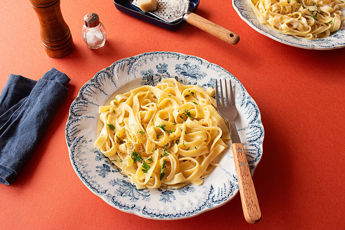 Eine Nahaufnahme von Fettuccine Alfredo auf einem roten Hintergrund. Garniert mit frischer Petersilie und geriebenem Parmesankäse