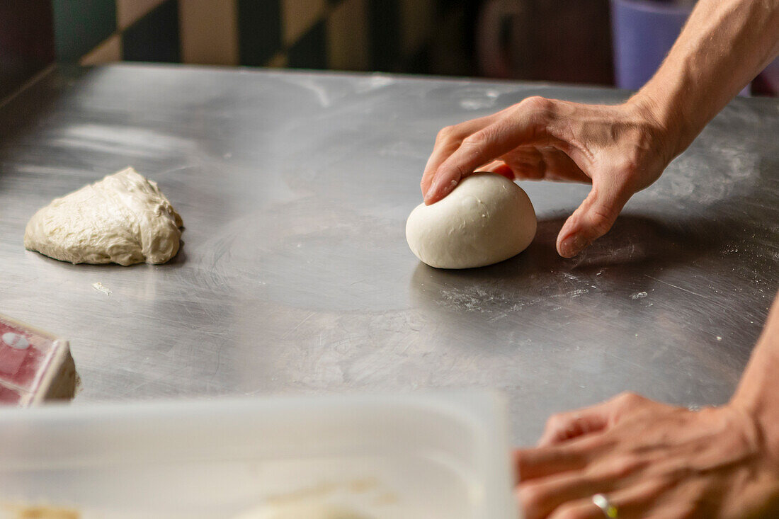 A detailed image capturing the hands of a person as they expertly knead pizza dough on a metallic kitchen surface, highlighting the pizza-making process