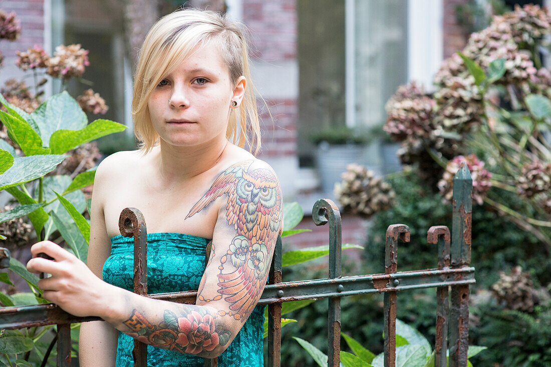 Porträt Junge Frau mit Tatoos im Garten eines Wohnhauses. Tilburg, Niederlande.