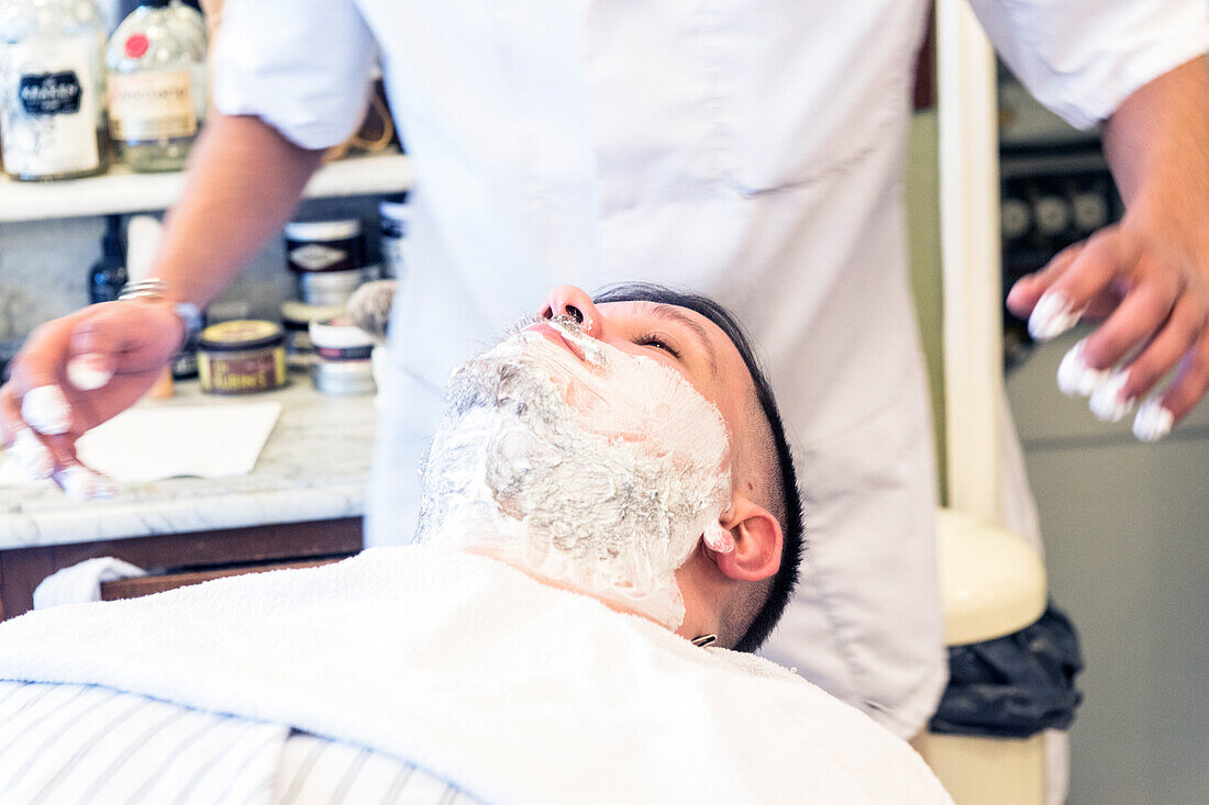 Friseur und Haarschneider bei der Rasur eines Kunden im Schorem Barber Shop im Nieuwe Binnenweg, Rotterdam, Niederlande.