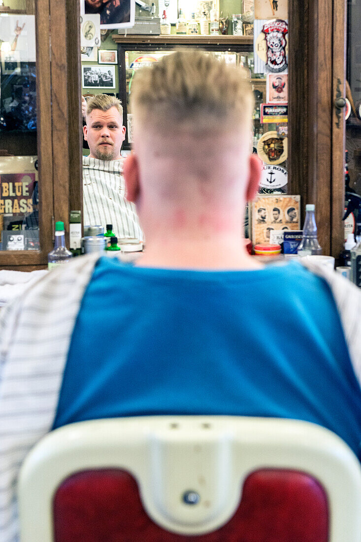 Junger Erwachsener, männlicher Kunde, der bei Schorem Barber Shop auf die Fertigstellung seines Haarschnitts wartet. Nieuwe Binnenweg, Rotterdam, Niederlande.