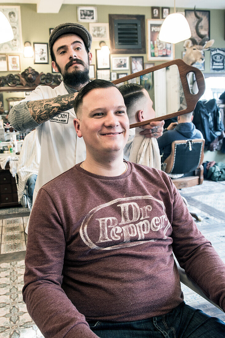 Professioneller Friseur und Haarschneider bei der Pflege der Frisur seines Kunden im Schorem Barber Shop am Nieuwe Binnenweg, Rotterdam, Niederlande.