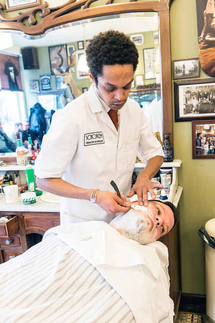 Professioneller Barbier und Haarschneider rasiert seinen Kunden im Schorem Barber Shop am Nieuwe Binnenweg, Rotterdam, Niederlande.