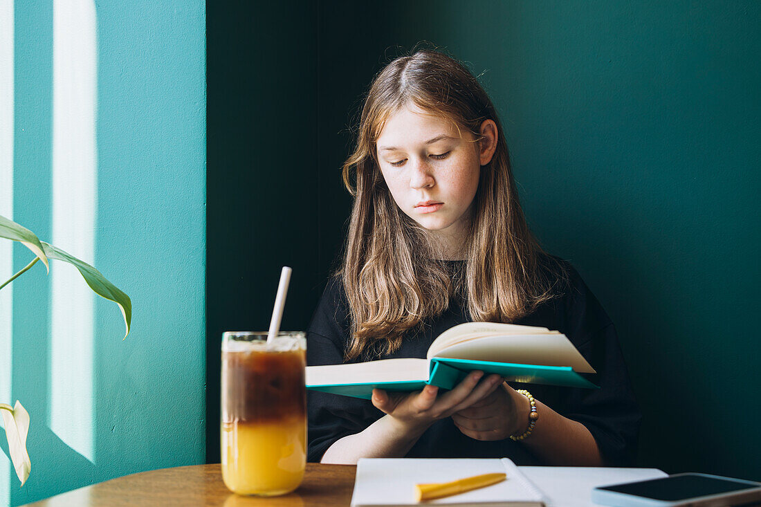 Eine fokussierte Studentin verbringt ihre Studienzeit in einem Café und schaut aufmerksam auf ein Buch hinunter