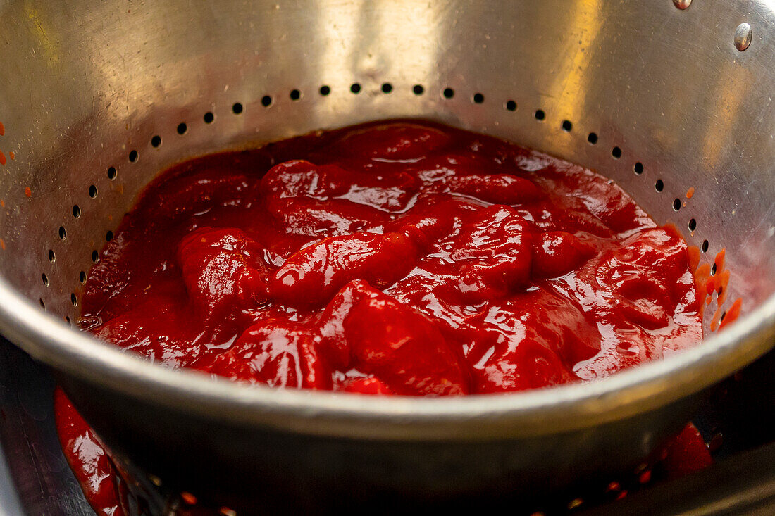 Leuchtend rote Tomatensoße, reichhaltig und stückig, liegt in einem Metallsieb, das die frühen Stadien der Zubereitung einer hausgemachten Pizza verdeutlicht