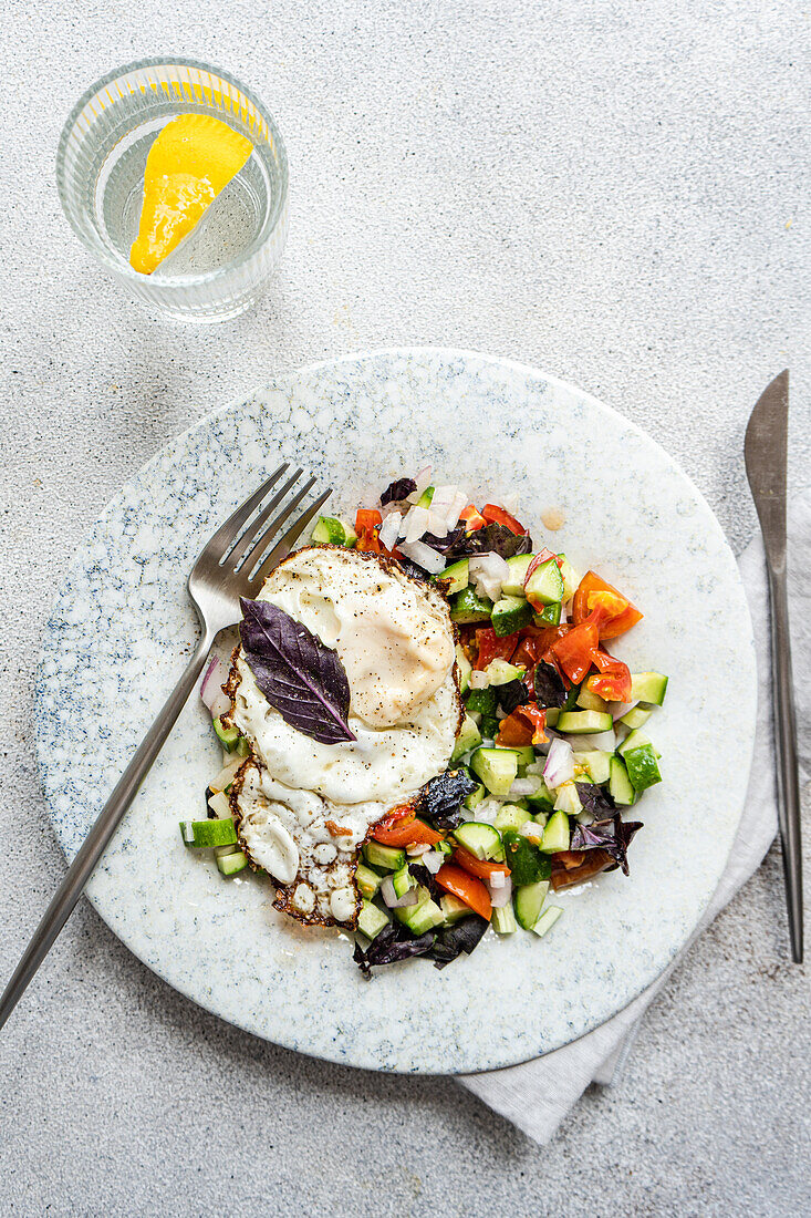 Ein nahrhaftes, ketofreundliches Mittagessen auf einem marmorierten Teller mit einem perfekten Ei auf einem bunten Salat aus Gurken, Tomaten und lila Basilikum