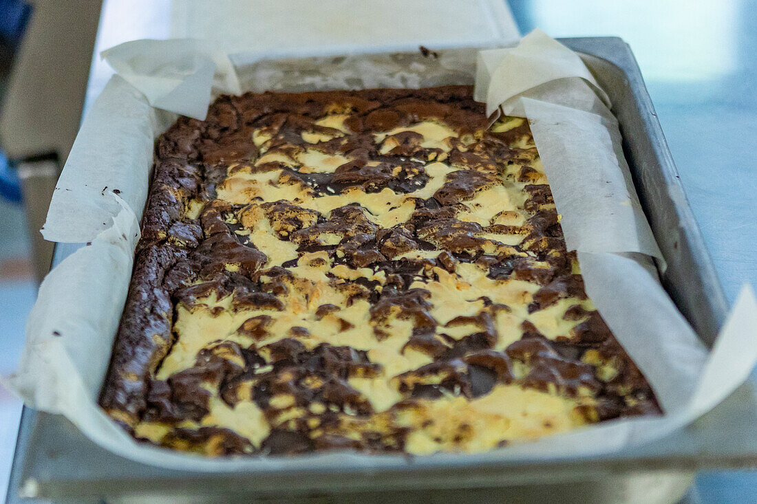 A metal tray featuring freshly baked marbled brownie with swirls of vanilla and chocolate batter, lined with parchment paper