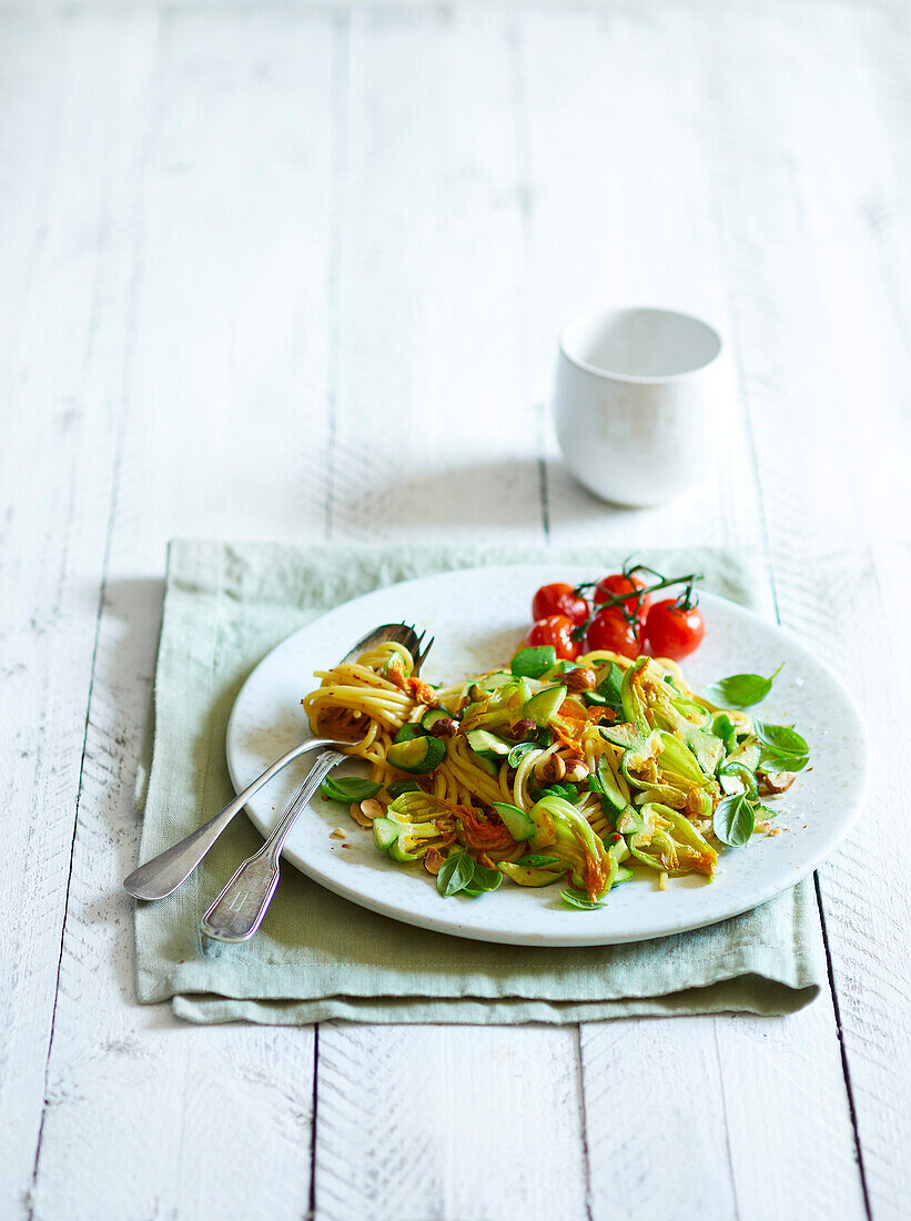 Fried courgette flowers, fried cherry tomatoes, basil and chopped hazelnuts, served with spaghetti on a white wooden background