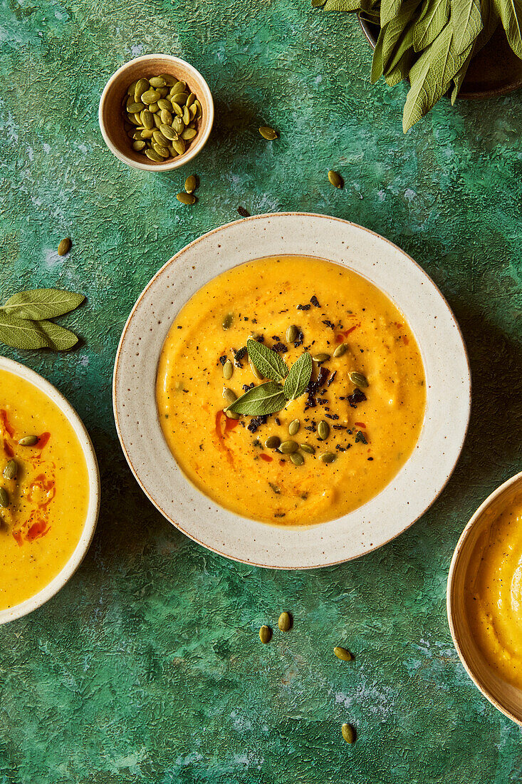 Pumpkin soup on a green surface with sage and pumpkin seeds