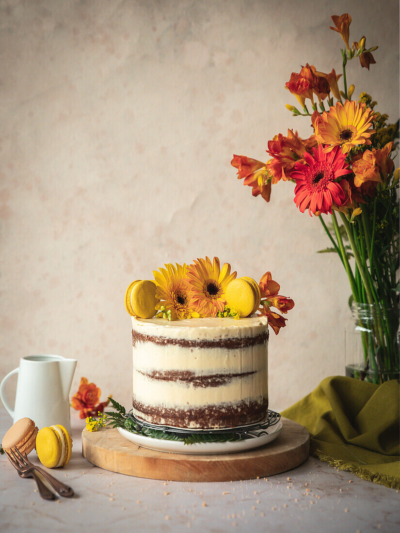 Decorated cake with a bouquet of flowers in shades of yellow and orange on a wooden board and a pair of macaroons.