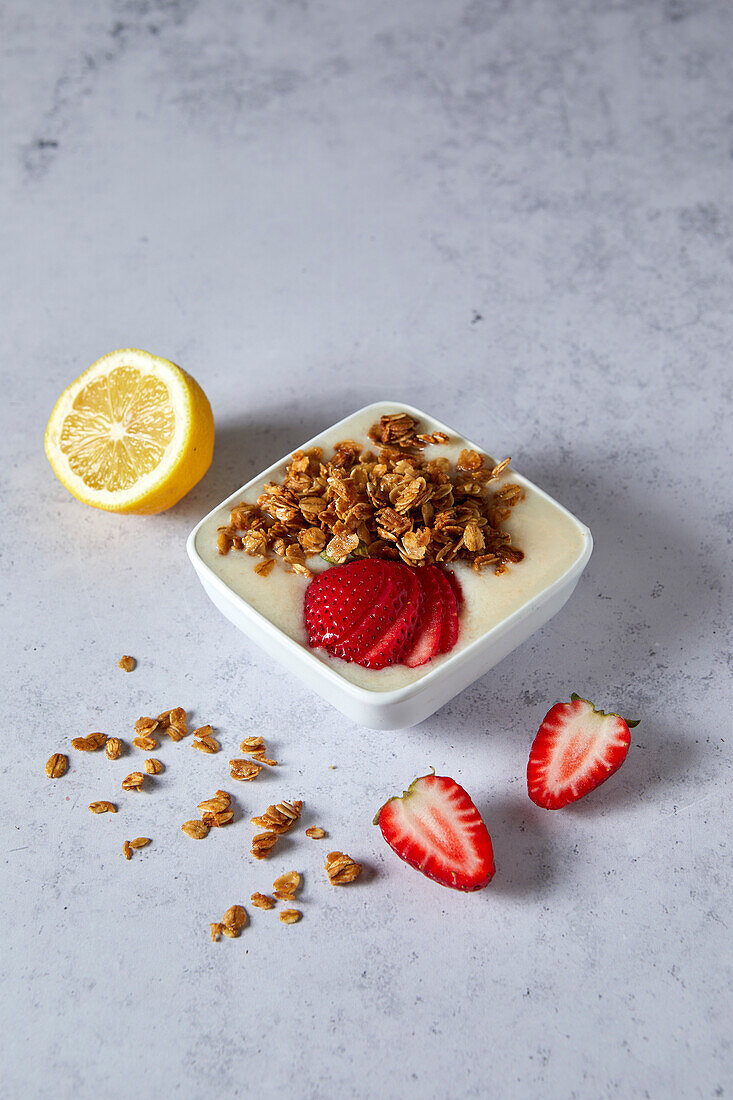 Bowl of lemon and strawberry smoothie with granola on a neutral background with soft shadows