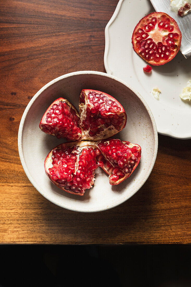 Pomegranate in ceramic bowl on wooden table.