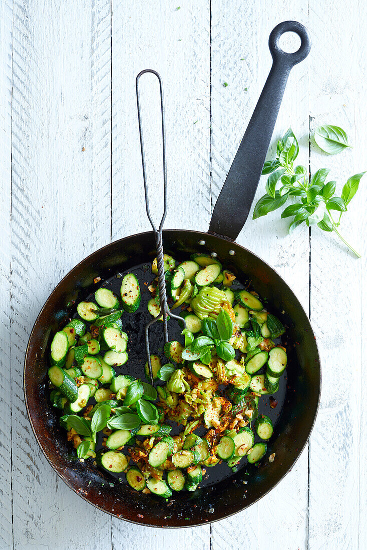 Fried zucchini flowers with basil, in a black pan, on a white wooden background