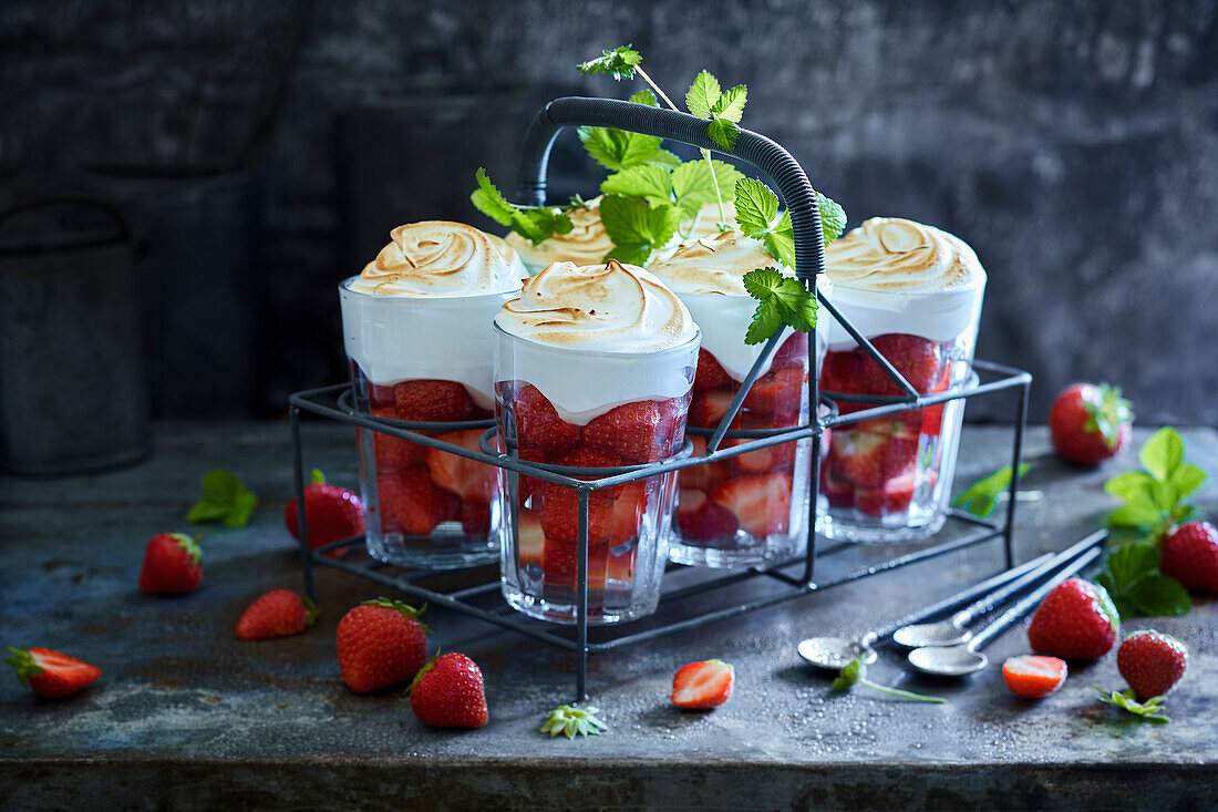 Six strawberry-filled glasses with meringue topping on grey metal background