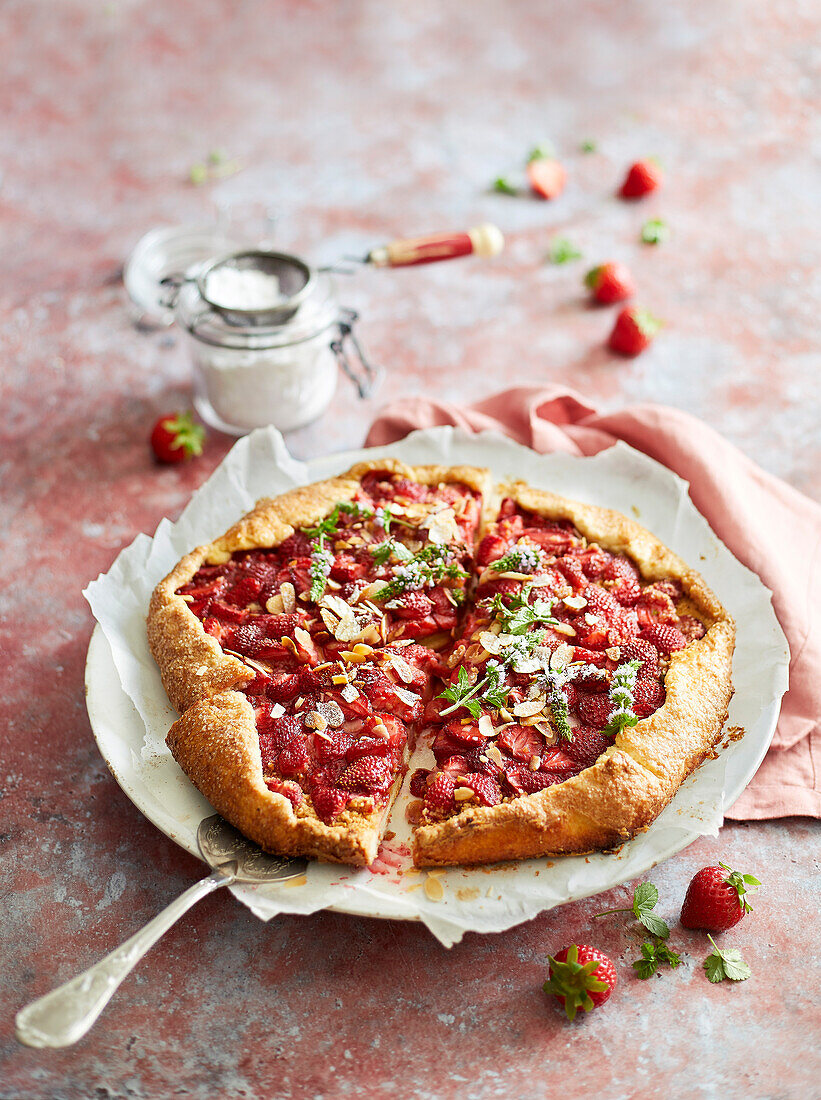 Cut-out strawberry galette on a red background, decorated with icing sugar and strawberries